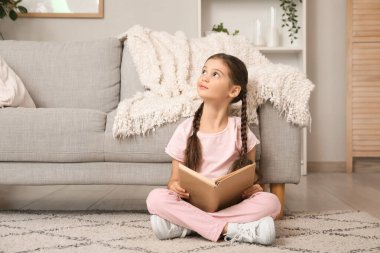 Kitapla evde oturan düşünceli küçük kız.