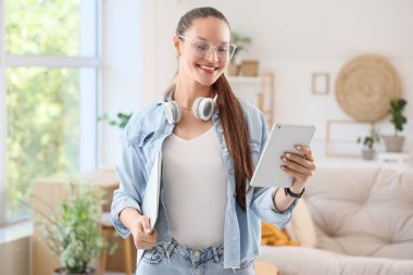 Evde dizüstü bilgisayarı ve tableti olan genç bir kadın var.