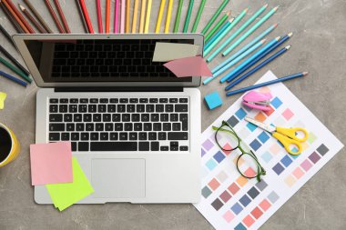 Gri grunge tablosunda dizüstü bilgisayarı, kalemleri ve renk çizelgeleri olan grafik tasarımcılarının çalışma yeri