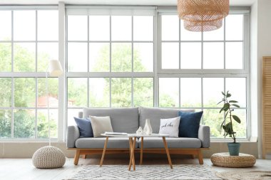 Pencerenin yanında gri kanepesi ve sehpası olan modern oturma odasının içinde.