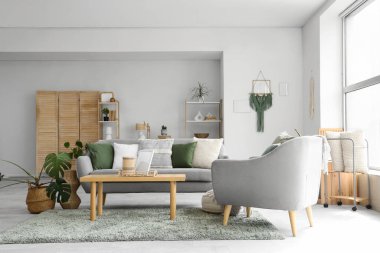 Gri kanepeli, kahve masalı, çiçekli ve koltuklu aydınlık oturma odasının içi.