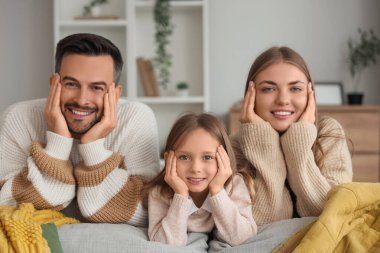 Küçük kız ve ailesi evde ekose kumaşlarla kanepede yatıyorlar.