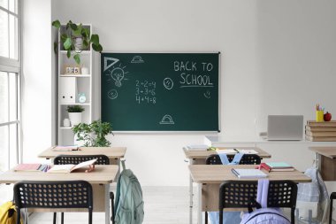 Okul sıraları olan boş sınıfın içi ve karatahtadaki okula geri dönüş metni