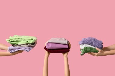 Pembe arka planda farklı giysi yığınları olan birçok kadın eli.