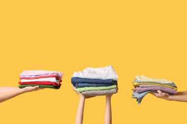 Sarı arka planda farklı giysi yığınları olan birçok kadın eli var.