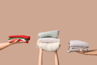 Bej arka planda farklı giysi yığınları olan birçok kadın eli