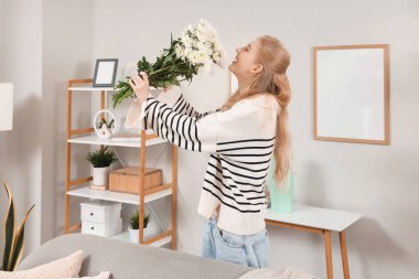 Evinde bir buket beyaz kasımpatı çiçeğiyle güzel, genç, mutlu bir kadın.
