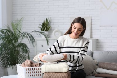 Evdeki masada kalın kazaklar katlayan genç bir kadın.