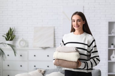 Evde bir yığın kalın kazağı olan genç bir kadın var.