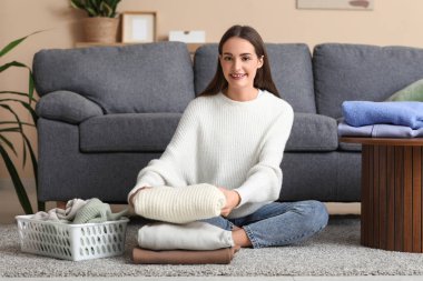 Evde yerde oturan sıcak süveter yığınıyla genç bir kadın.