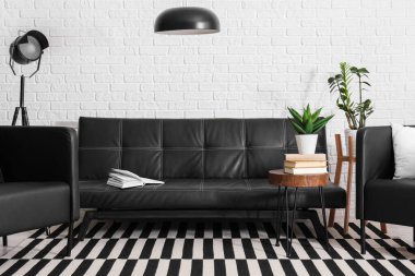 Siyah deri kanepe, sehpa, koltuk ve lambalar oturma odasında.