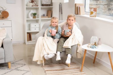 Ekoseli küçük bir çocuk ve kız kanepede oturup evde çay içiyor.