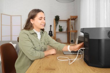 Ofisteki portatif elektrik santraliyle dizüstü bilgisayarı şarj eden genç bir kadın.
