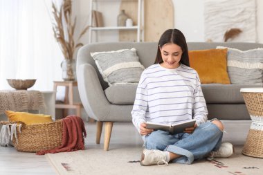 Güzel, genç, mutlu bir kadın evde kitap okuyor.