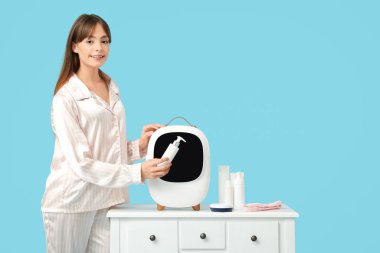 Mavi arka planda kozmetik ürünleri için küçük buzdolabı olan güzel genç bir kadın.