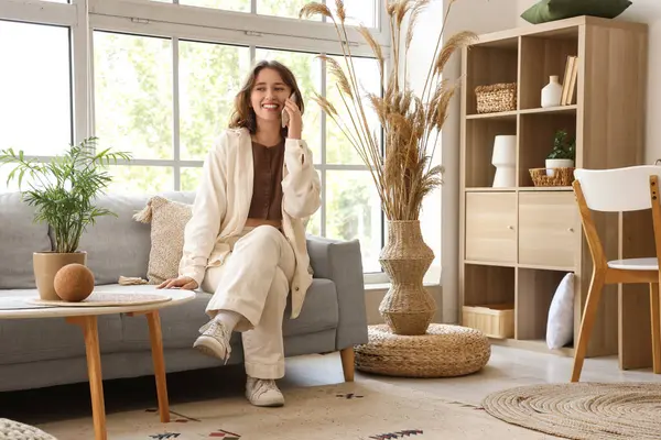 Oturma odasındaki koltukta cep telefonuyla konuşan genç bir kadın.