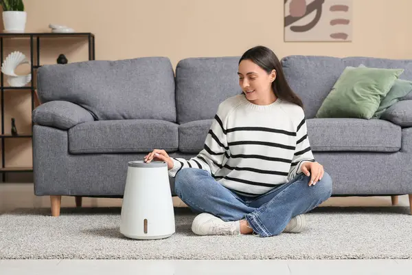 Evdeki halının üzerinde modern hava nemlendiricisi olan güzel genç bir kadın oturuyor.
