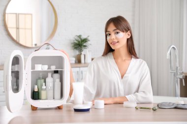 Küçük buzdolabı ve kozmetik ürünleriyle banyoda güzel bir genç kadın.