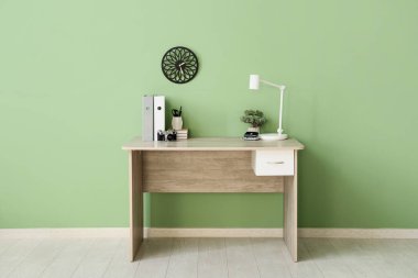 Ofisteki yeşil duvarın yanında klasörleri, lambası ve kırtasiyesi olan şık bir iş yeri