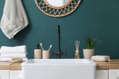 Lavabo ve banyo aksesuarları banyodaki yeşil duvarın yanında.