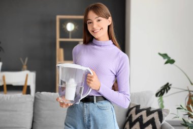 Evde su filtresi taşıyan genç bir kadın var.