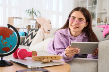 Otelde tablet bilgisayarlı rezervasyon odası olan kadın turist evdeki kanepede oturuyor.