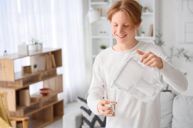 Genç adam evdeki filtre sürahisinden bardağa su dolduruyor.