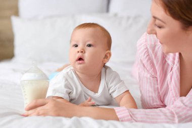 Bir şişe sütü olan genç bir anne ve küçük bebeği yatak odasında uzanıyorlar.