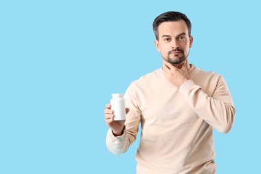 Elinde ilaç şişesi olan yakışıklı bir adam mavi arka planda tiroit bezini inceliyor.