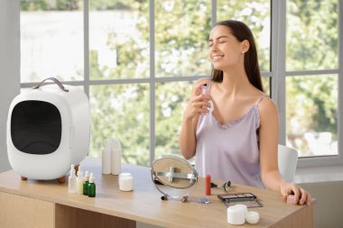 Küçük buzdolabı ve evde parfüm kullanan mutlu genç bir kadın.