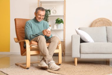 Cep telefonlu yaşlı adam evdeki koltukta oturuyor.