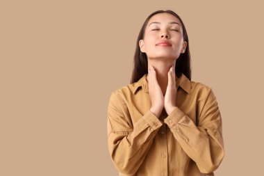 Genç Asyalı kadın bej arka planda tiroit bezini inceliyor.