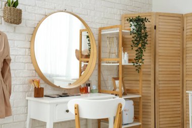 Kozmetik ürünleri, aksesuarlar ve ışıklı tuğla duvarda asılı ayna olan giyinme masası.