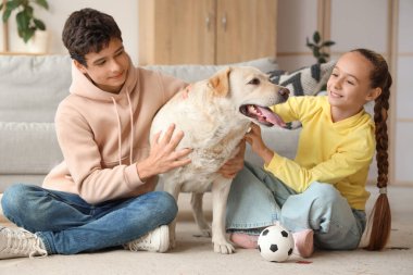 Mutlu kız ve erkek kardeş ve şirin Labrador köpeği evde yerde oturuyor.
