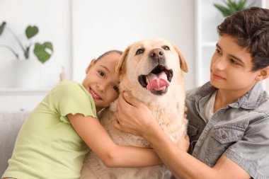 Mutlu kız ve erkek kardeş evde Labrador köpeğine sarılıyor.
