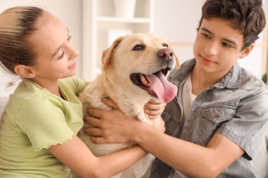 Mutlu kız ve erkek kardeş evde Labrador köpeğine sarılıyor.