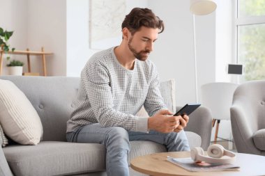 E-okuyuculu genç adam evdeki kanepede oturuyor.