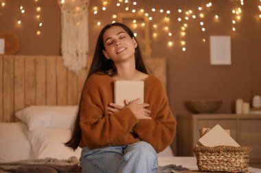 Güzel, genç, mutlu bir kadın, elinde kitapla, akşam saatlerinde parlayan ışıklara karşı bankta oturuyor.