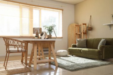 Oturma odasının içinde programcı masası, kanepesi ve raf ünitesi var.