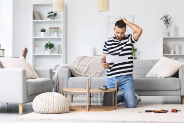 Evde kahve masasını elle monte eden sorunlu bir genç adam.