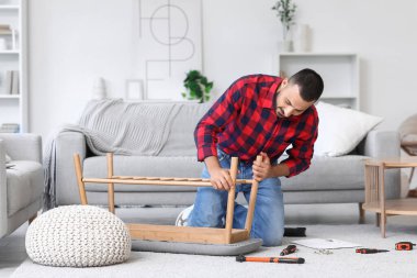 Genç adam evdeki bankta toplanıyor.