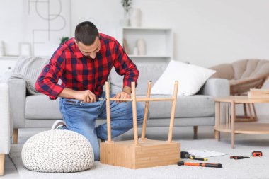 Tornavidalı genç adam evde ahşap masa kuruyor.