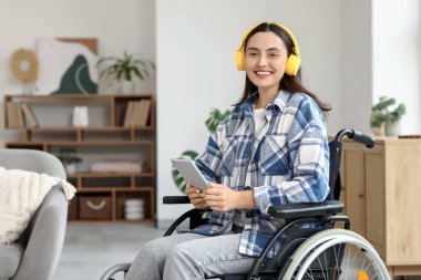 Evde kulaklığı ve tablet bilgisayarı olan tekerlekli sandalyedeki genç kadın.