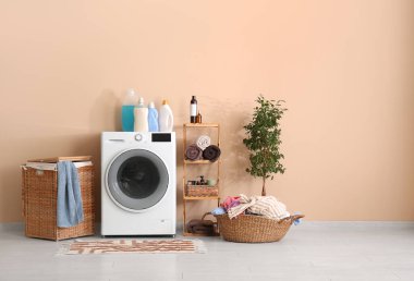 Modern çamaşır makinesi, çamaşır sepeti, raf ünitesi ve dekoratif ağaç.