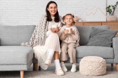 Anne ve küçük kızı ekose giyip oturma odasında içecek içiyorlar.