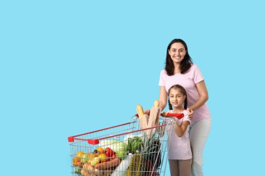 Güzel, genç, mutlu anne ve kızı mavi arka planda alışveriş arabasıyla.