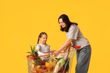 Güzel, genç, mutlu anne ve kızı sarı arka planda alışveriş arabalarıyla.