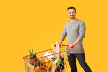 Sarı arka planda alışveriş arabası olan mutlu genç bir adam.