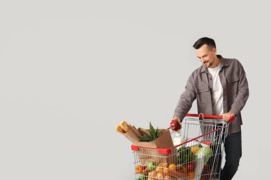 Gri arka planda alışveriş arabası olan mutlu genç bir adam.