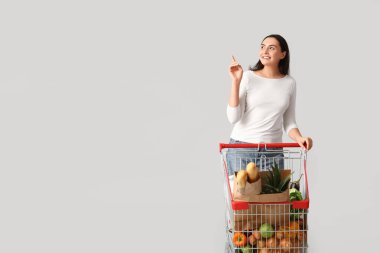 Güzel, genç ve mutlu bir kadın alışveriş arabasıyla gri arka plandaki bir şeyi işaret ediyor.